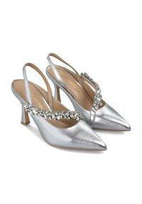 Tacchi slingback metallici argento con punta appuntita, accentuati da una fascia gioiello sul davanti e un tacco sottile di altezza media.