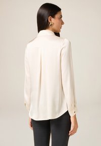Crèmekleurige blouse met lange mouwen, een plissé aan de achterkant, geribbelde manchetten en een afgeronde zoom. Soepele textuur en lichtgewicht stof.