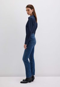 Camicia blu navy abbottonata abbinata a jeans blu aderenti. Stivali neri con tacco alla caviglia completano il look. Tessuto morbido e vestibilità su misura.