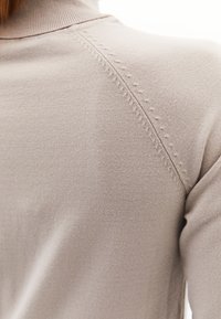 Lichtbeige top met een hoge halslijn, een gladde textuur en decoratieve stiksels langs de schoudernaad.