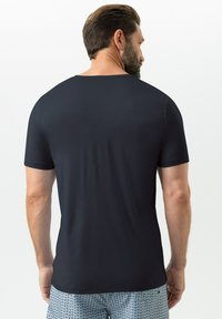 T-shirt à manches courtes pour homme, bleu marine foncé, col rond, tissu lisse, porté avec un short à motifs, détail de couture visible à l'ourlet.