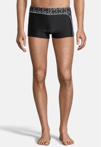Shorts de bain noirs avec une taille à motifs et des accents blancs sur les côtés. Longueur courte, fabriqués en matériau lisse et extensible.