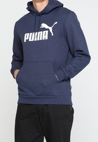Felpa con cappuccio blu navy realizzata in tessuto morbido, con una tasca a marsupio frontale e un logo Puma bianco stampato sul petto.