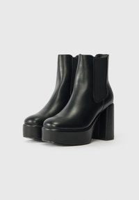 Par de botines de plataforma de cuero negro con tacones de bloque y paneles laterales elásticos sobre un fondo blanco.