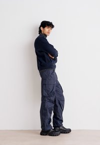 Felpa blu navy con orlo a coste abbinata a pantaloni cargo leggeri e resistenti all'acqua, dotati di multiple tasche e vestibilità rilassata.