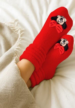 Red fleece socks with ribbed cuffs, featuring a black-and-white Minnie Mouse design and red bow accents, against a light background.