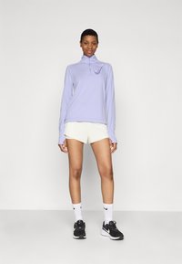 Lys lilla langermet treningstopp med kvart glidelås og hvit swoosh-logo, sammen med hvite shorts og svarte joggesko.