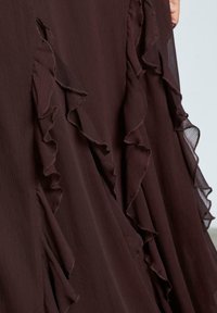 Abito bordeaux scuro con volant sovrapposti lungo il lato, realizzato in tessuto leggero e testurizzato con una finitura trasparente ai bordi.