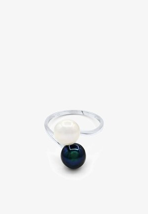 Bague ouverte en argent avec deux perles, une blanche et une noire, positionnées en face l'une de l'autre sur l'anneau.