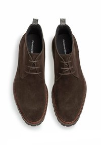 Braune Wildleder-Stiefeletten mit glatter Oberfläche, runder Zehenpartie, Schnürdesign und kontrastierenden braunen Nähten entlang der Sohle.