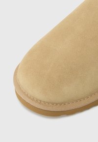 Stivale in suede con una morbida tomaia beige, punta arrotondata e cuciture a contrasto. Presenta una suola in gomma texturizzata per grip e durata.