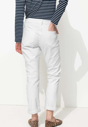 Jeans blancs à revers, avec des poches arrière, montrés de l'arrière. Associés à un haut à manches longues rayé bleu marine et blanc et des ballerines à imprimé animal.