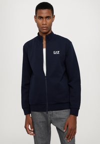 Felpa zip-up blu navy realizzata in tessuto misto cotone, con colletto alto, polsi a coste e logo EA7 bianco ricamato sul petto.