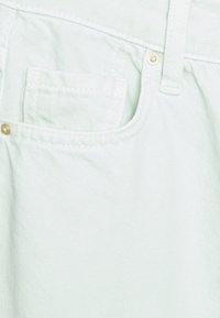 Tecido de ganga verde-claro com um pequeno bolso frontal, detalhes em costura e um botão metálico decorativo. Textura suave com ligeira elasticidade.