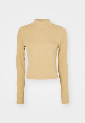 Dolga majica s turtleneck ovratnikom, rebrasta v svetlo bež barvi s slim fit krojem. Ima majhen zlat Nike logotip na prsih. Gladka tekstura.