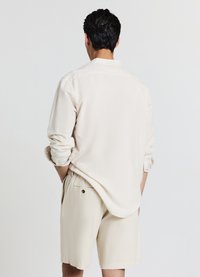 Light beige button-up shirt with rolled sleeves, paired with matching beige shorts featuring a side pocket and button detail.