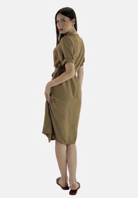 Brun, knälång klänning med korta rullade ärmar och ett bälte i midjan, med en sidoklyvning och mjuk tygstruktur.