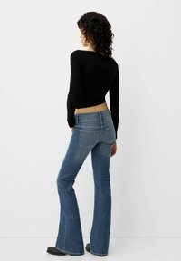 Schwarzes Langarmoberteil, kombiniert mit blauen Schlagjeans. Das Outfit zeichnet sich durch eine taillierte Silhouette und strukturierten Denim mit Gesäßtaschen aus.