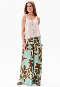Beige linnen tanktop met knopen, gecombineerd met vloeiende mintgroene wijde broek met grote bruine bloemmotieven.