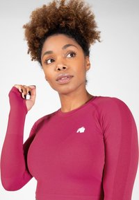 Bordeaux langarm sportshirt met een aansluitend ontwerp, gestructureerde mouwen en een klein wit logo op de borst. Glad stoffen afwerking.