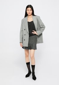 Grå pinstripet oversized blazer, svart knappet topp, grå plissett miniskjørt, svarte gjennomsiktige sokker, svarte spisse hæler.
