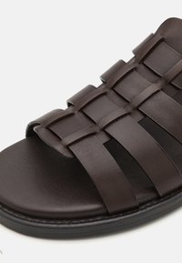 Ruske nahkalenkkarit, joissa on kudottu hihnadesign, avoin kärki ja litteä pohja. Pinnassa on sileä rakenne, jossa on hieno kiilto.