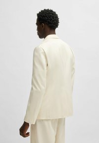 Light ivory blazer with a tailored fit, featuring notched lapels and a smooth texture. Shown from the back, with slight shoulder padding.