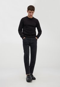 Maglione nero a maglia e pantaloni slim-fit scuri. Tessuto strutturato e gambe dritti. Scarpe nere stringate con suole spesse e design minimalista.