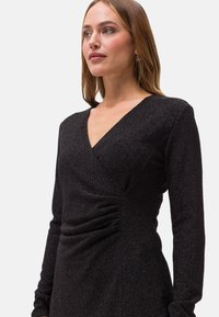 Schwarzes langärmeliges Kleid mit tiefem V-Ausschnitt, Wickeldesign und strukturiertem Stoff mit gerafften Details an der Taille.