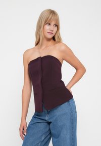 Burgundy strapless top with a structured bodice, featuring a front pleat detail and two side pockets, paired with light blue wide-leg jeans.