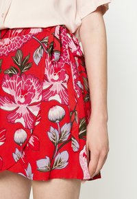 Gonna rossa floreale con grandi fiori rosa e bianchi, dotata di dettaglio in vita legato e tessuto leggero e testurizzato.