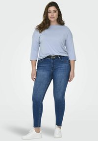 Lyseblå, løs topp med trekvart lange ermer, sammen med mørkeblå skinny jeans. Hvite joggesko og et svart belte med en rund spenne.