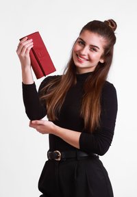 Red wallet with an embossed zigzag pattern, made of smooth leather, held in a hand against a plain white background. Black long-sleeve shirt.