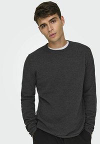 Donkergrijze lange mouwen shirt van een textuurstof, met een ronde halslijn en een licht gebogen zoom. Draagt over een witte T-shirt.