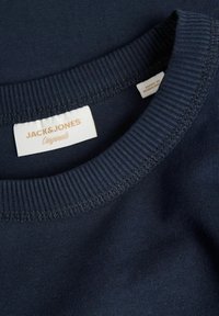 Navyblauwe katoenen T-shirt met een ribbelboord aan de ronde hals. Het label vermeldt "JACK & JONES Originals" in gouden letters, met zichtbare stiksels rond de hals.