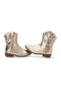Botas tobilleras metálicas doradas con un acabado suave, punta redondeada, cremallera lateral y detalle decorativo de flecos en el lado exterior. Tacón bajo y apilado.