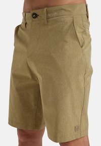 Beige shorts made of textured fabric, featuring side pockets, a button closure, and a small logo patch on the hem.