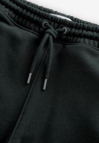 Pantalones deportivos negros con una tela texturizada, que cuentan con una cinturilla elástica y un cordón con puntas metálicas para ajuste.