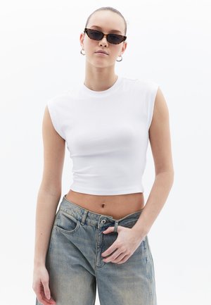 Top corto bianco a coste con cuciture sulle spalle, abbinato a jeans di denim azzurri chiari, morbidi e comodi. Nessun motivo o dettaglio visibile.