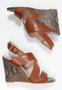 Sandali con tacco wedge in pelle marrone, con cinturini incrociati, tacco wedge in stampa serpente testurizzata e cinturino regolabile alla caviglia. Fodera interna liscia.