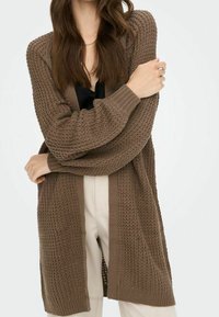 Cardigan lavorato a maglia di un ricco colore marrone, con una trama testurizzata e design aperto sul davanti. Tessuto morbido con polsini e orlo a costine.