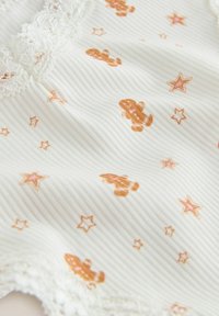 Biely textil s jemnými vertikálnymi pruhmi, s potlačou oranžových medvedíkov a ružových hviezd, lemovaný jemným čipkovým okrajom.