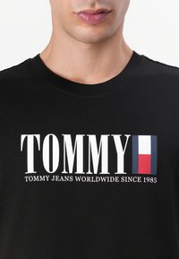 Svart bomulls t-skjorte med stor hvit "TOMMY" tekst og design av det franske flagget. Delt med teksten "TOMMY JEANS WORLDWIDE SINCE 1985".