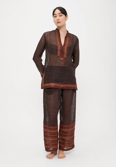 Hnedá priesvitná dlhá tunika s výstrihom do V a vertikálnymi pruhovanými akcentmi. Kombinovaná s voľnými nohavicami v rovnakom dizajne so pruhovanými manžetami.