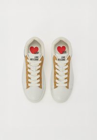 White and tan sneakers featuring a smooth leather upper and suede accents, with a printed logo on the tongue and colorful insoles.