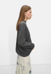 Szary sweter dziany z okrągłym dekoltem i opuszczonymi ramionami, połączony z jasną kremową spódnicą z niebieskimi wzorami.