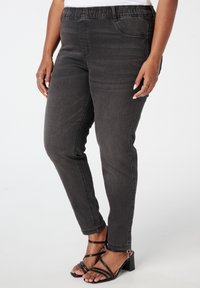 Zwarte denim broek met een stretchy tailleband, slim fit, zichtbare stiksels en zijzakken. Gecombineerd met zwarte strappy hoge hakken.