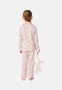 Ensemble de pyjama à motif floral en tissu doux, présentant des fleurs roses, bleues et vertes. Comprend un haut avec col et un pantalon assorti. Enfant tenant un jouet.