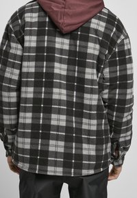 Veste en flanelle noire et grise à motif à carreaux, dotée d'une capuche bordeaux et d'une texture douce, vue de dos.