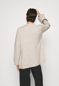 Beige knitted sweater with a relaxed fit, long sleeves, and a slightly longer back hem. Made of soft, textured fabric.